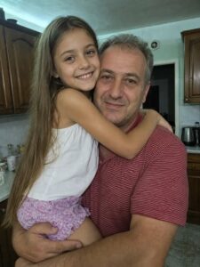 На тази снимка се усмихвах в прегръдките на втория си баща… Години наред майка ми вярваше, че той ме обича като собствена дъщеря. Но не знаеше, че зад затворени врати същите тези ръце ме подлагаха на жестоко насилие, чиито последици щяха да ме следват цял живот. 54 781206905 122258680232262165 3122532158106133013 n